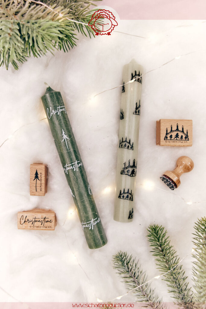 Zwei dekorativ bestempelte Stabkerzen auf weißem Untergrund. Eine grüne Kerze mit weißen Tannenbaumstempeln und dem Schriftzug ‚Christmastime', die andere hell mit schwarzen Schwibbogenstempeln. Im Hintergrund sind Stempel, grüne Tannenzweige und eine feine Lichterkette zu sehen.