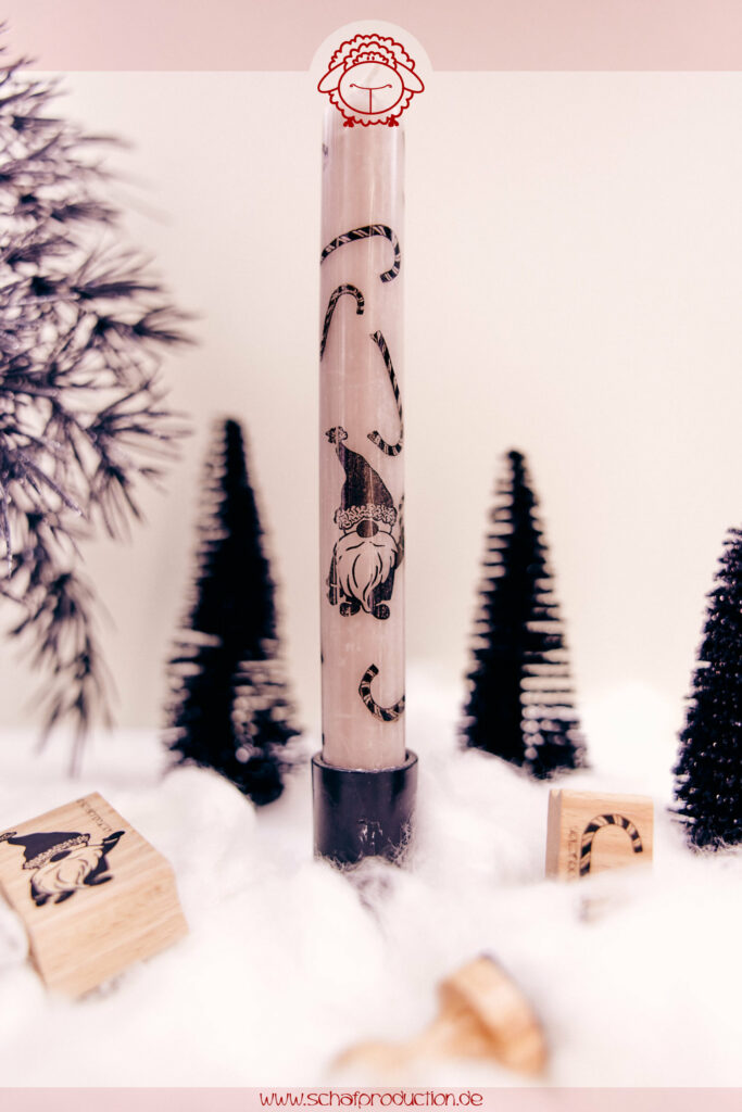 Schmale Stabkerze im Kerzenhalter, auf Watte-Schneeboden, bestempelt mit schwarzen Zuckerstangen und Weihnachtswichtel, umgeben von Stempeln, schwarzen Weihnachtsbäumen und dunklen Tannenzweigen.