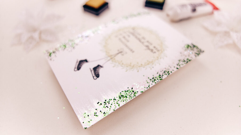 Weihnachtskarte mit der Einladung zum Schlittschuhlaufen, umrahmt von einem Mistelzweig-Kranz und verziert mit weißem und grünem Glitzer.