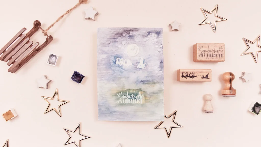 DIY Weihnachtskarte mit einem gestempelten Rentierschlitten, der um den Mond fliegt, erstellt mit Negativ-Embossing-Technik und Aquarellfarben