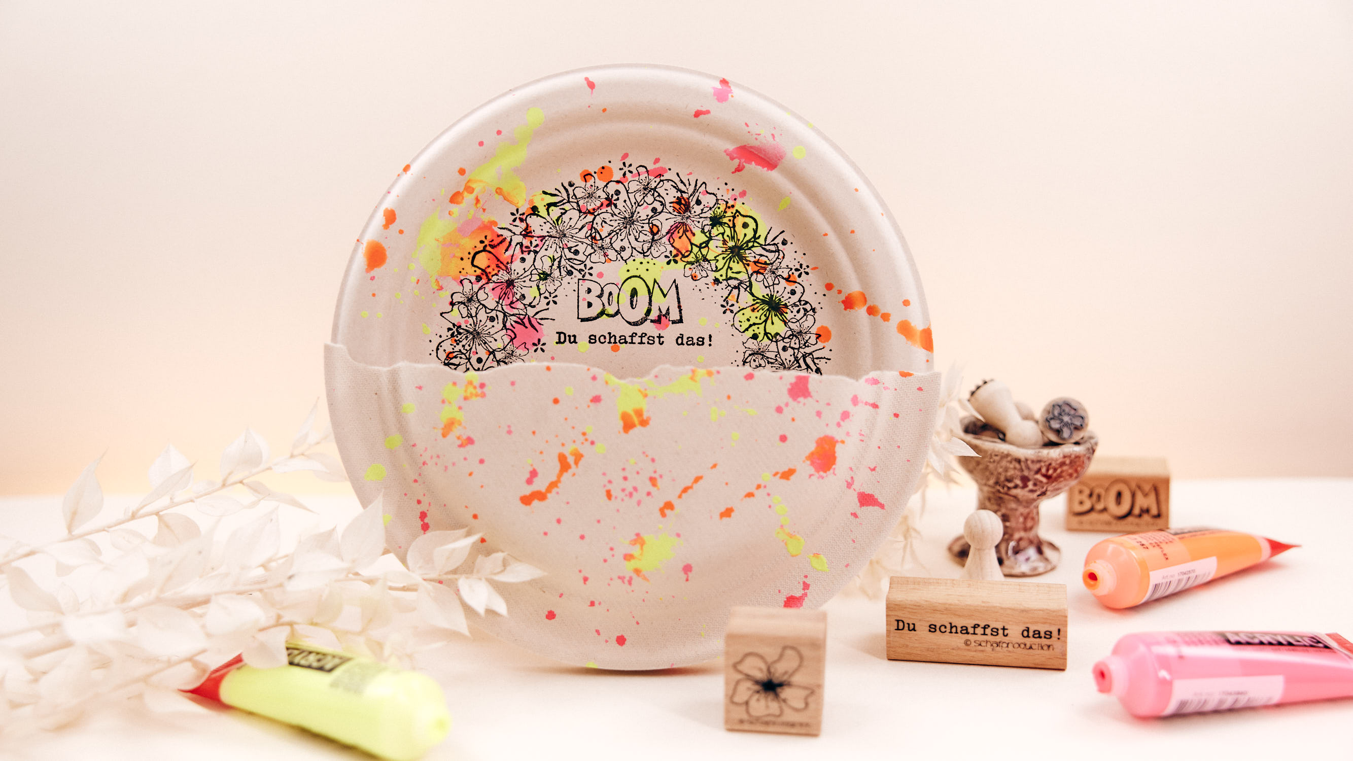 Geschenkverpackung-aus-Dekoteller-mit-Neonspritzern-und-Blumenkranz-Q